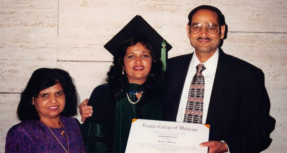 Woman in graduation gown with parents, holding diploma