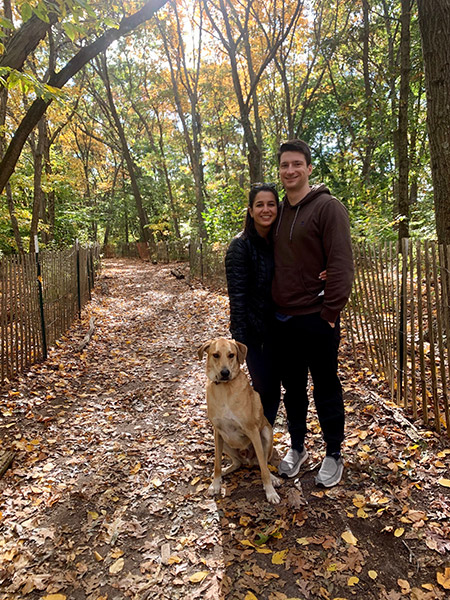 Man and woman with dog, surrounded by trees and falling leaves