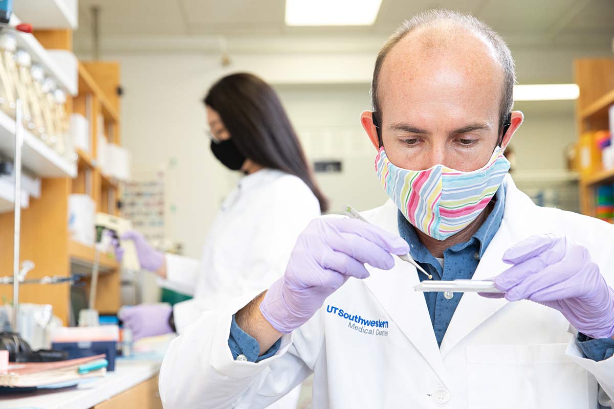 Man wearing mask in whtie lab coat, working with slide