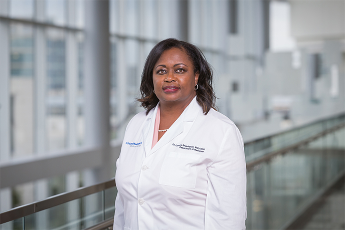 Woman wearing a labcoat in a glass-lined hallway