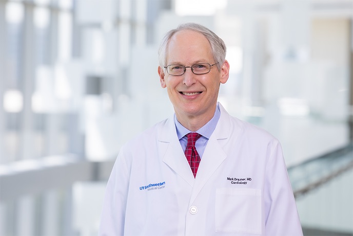 Man with lab coat, greying hair, standing in front of windows