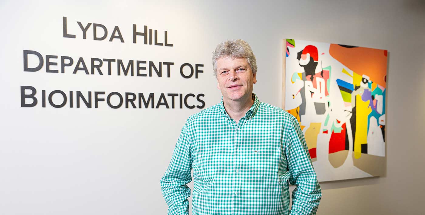 Man in green shirt standing by sign that reads Lyda Hill department of bioinformatics.