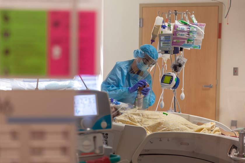 Person in scrubs, mask and face shield holding patient's hand