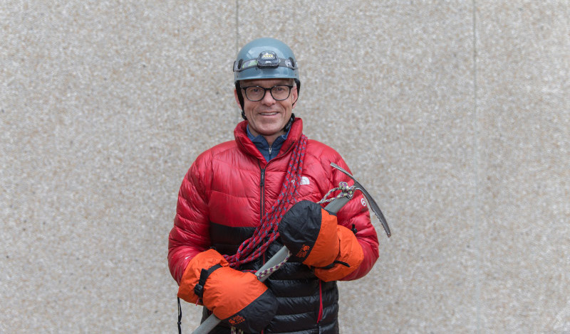 Man in helmet, jacket, holding climbing axe and other climbing gear