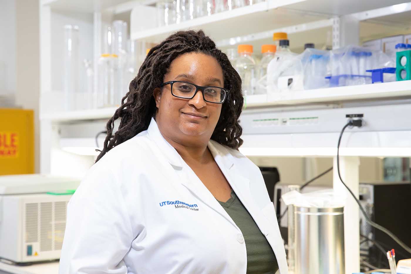 Woman with glasses, dark dreadlocks, wearing a lab coat and standing in a lab