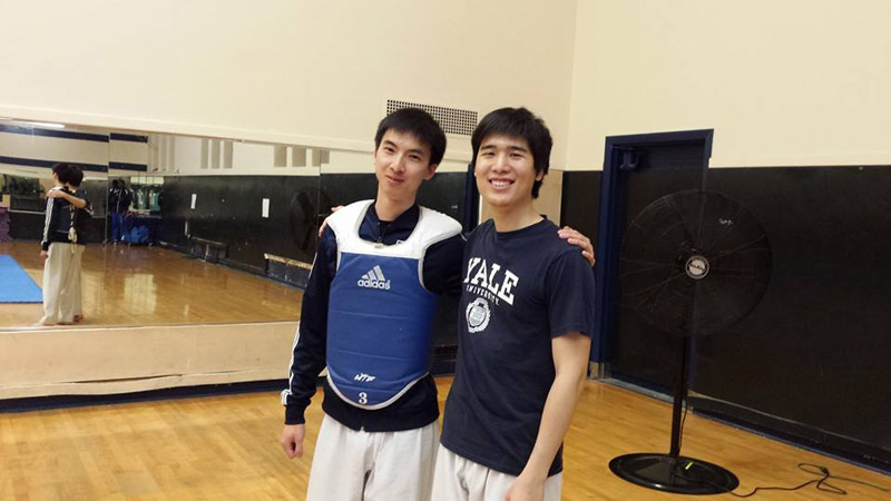 Two men, one wearing protective padding, in gym