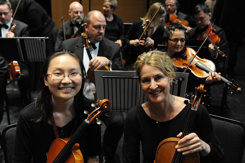 Two women holding violins smiling