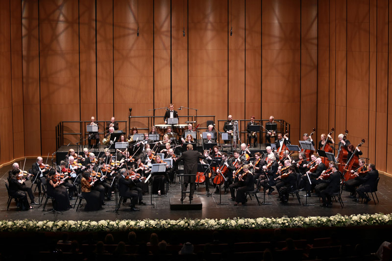 Orchestra playing on a stage with a wood background