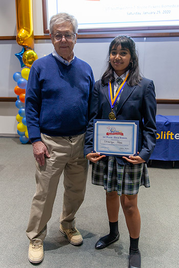 Man in blue sweater and girl in blue blazer holding a certificate pose for a photo
