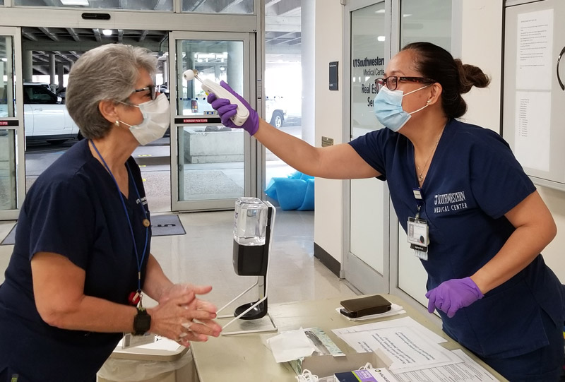 Woman in scrubs taking temperature reading from forehead of another woman in scrubs