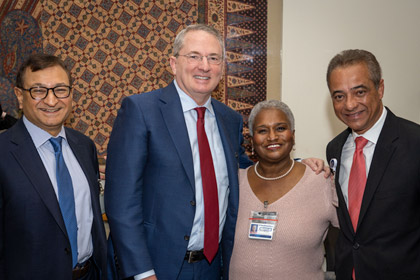 Woman in light pink dress smiling, next to three men in suits