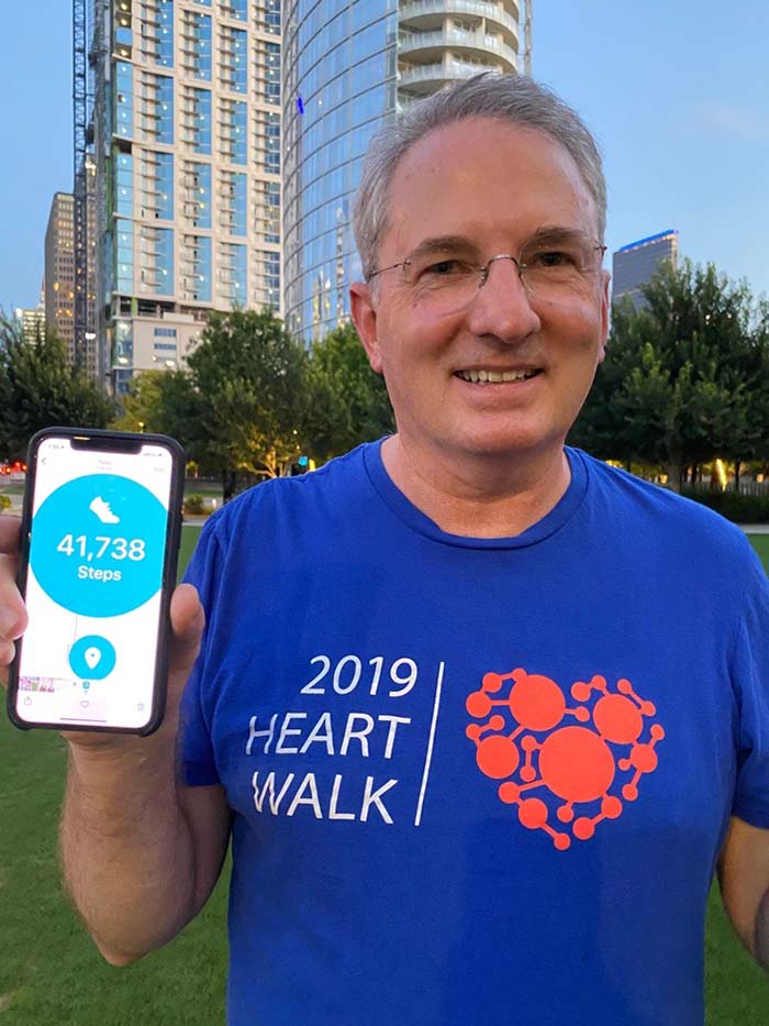 Man in blue 2019 heart walk, holding up phone