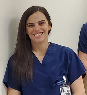 Woman with dark brown hair wearing blue scrub top