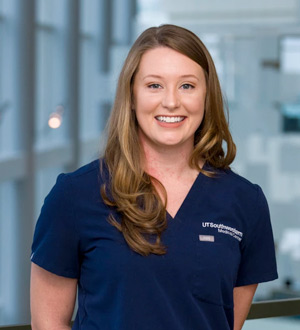 Woman with dark blonde hair wearing blue scrub top