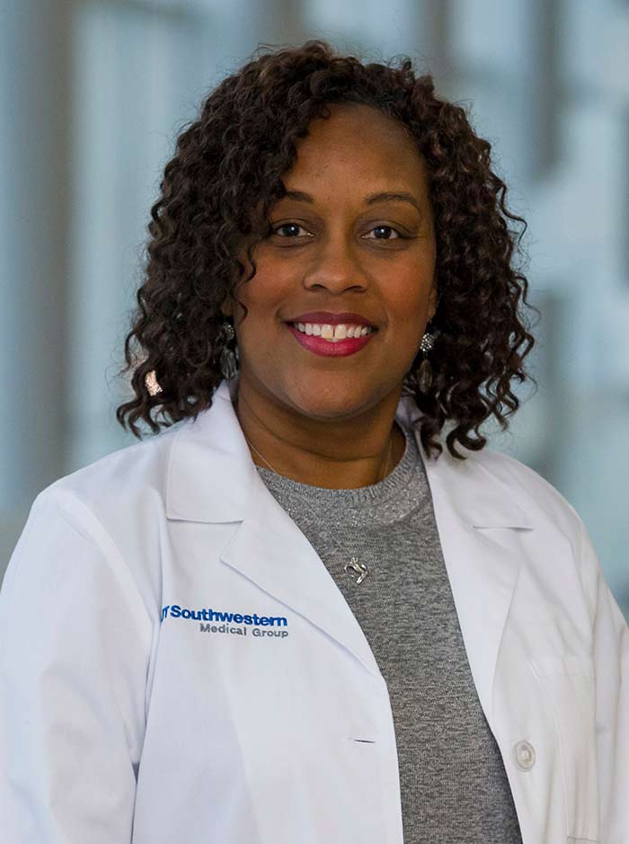 Woman with brown hair, wearing white lab coat and gray shirt