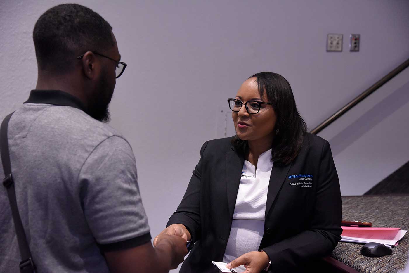 Woman in black blazer with UTSW logo on it talking to man