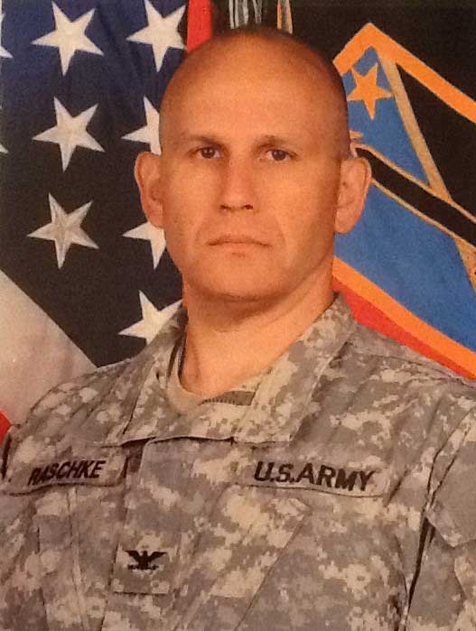 Man in front of flags wearing US Army uniform