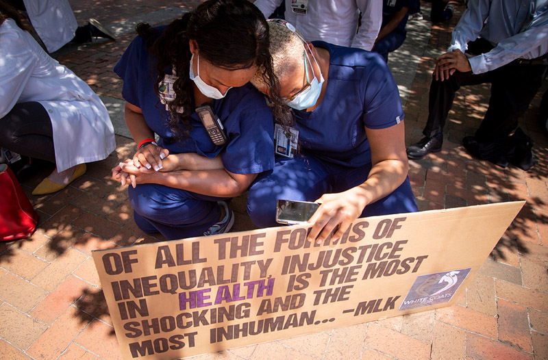 Two women in masks, holding sign and holding hands