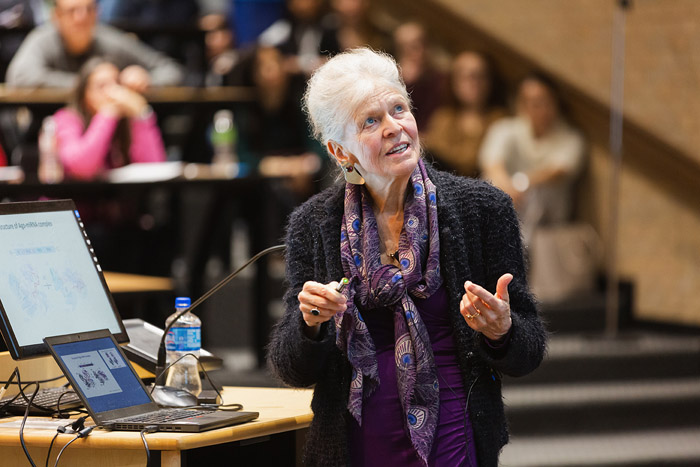 Woman with grey hair, purple scarf standing at podium