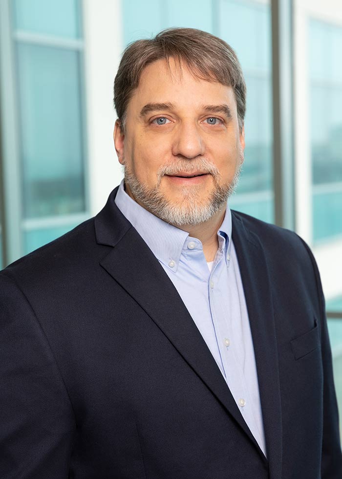 Man with beard, grey hair, wearing dark blue suit