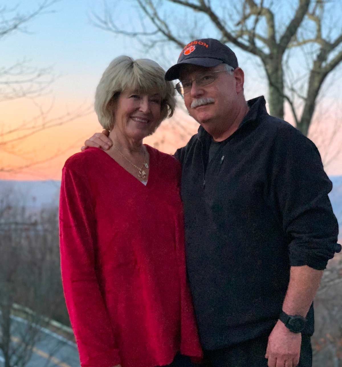 Man in jacket and woman in red sweater standing in front of sunset