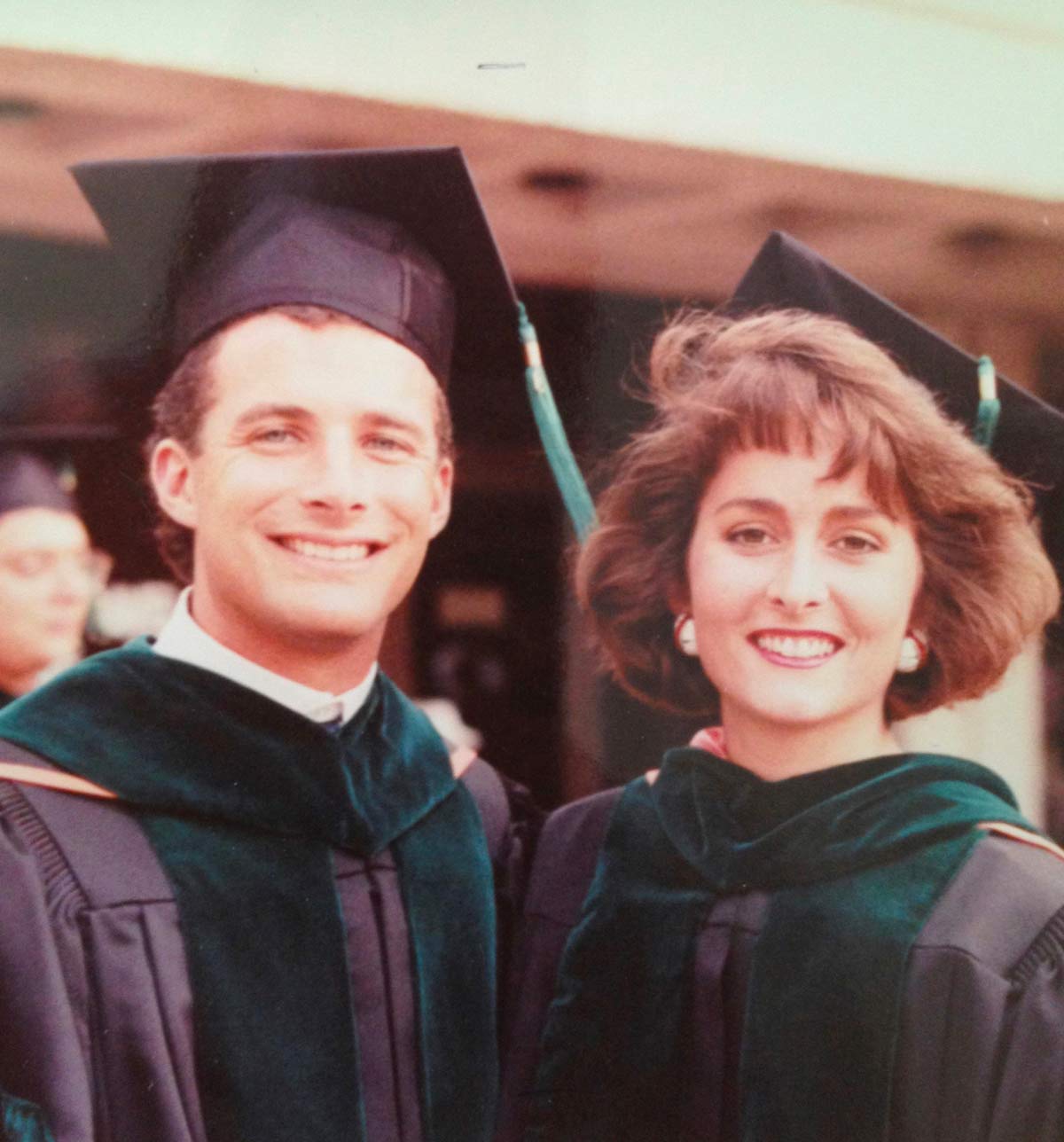 Man and woman in black graduation caps and gowns with dark green sashes.