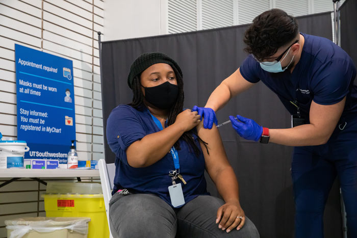 Person sitting in chair with mask on getting injected in shoulder.