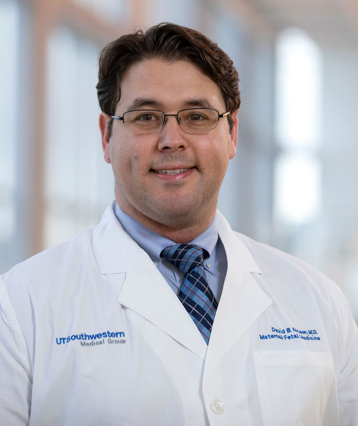 Man with dark hair, glasses, wearing white lab coat