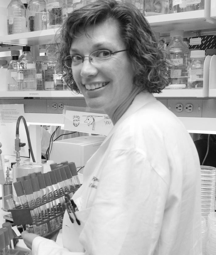 Black and white photo of woman in lab wearing lab coat