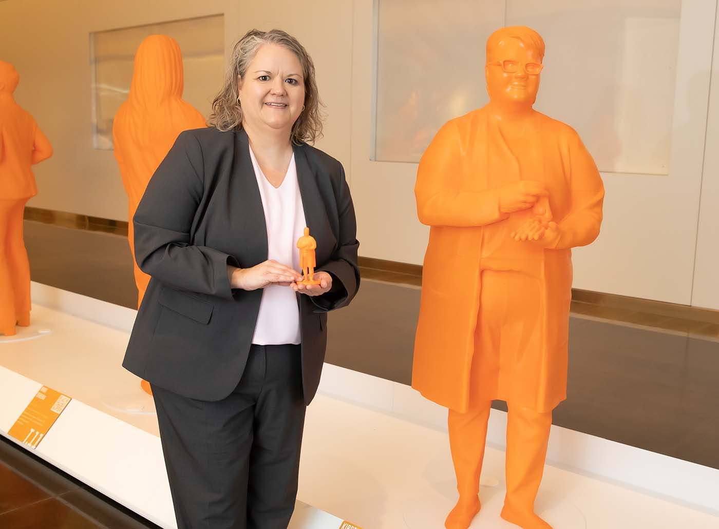 Woman in gray suite standing next to statue of herself