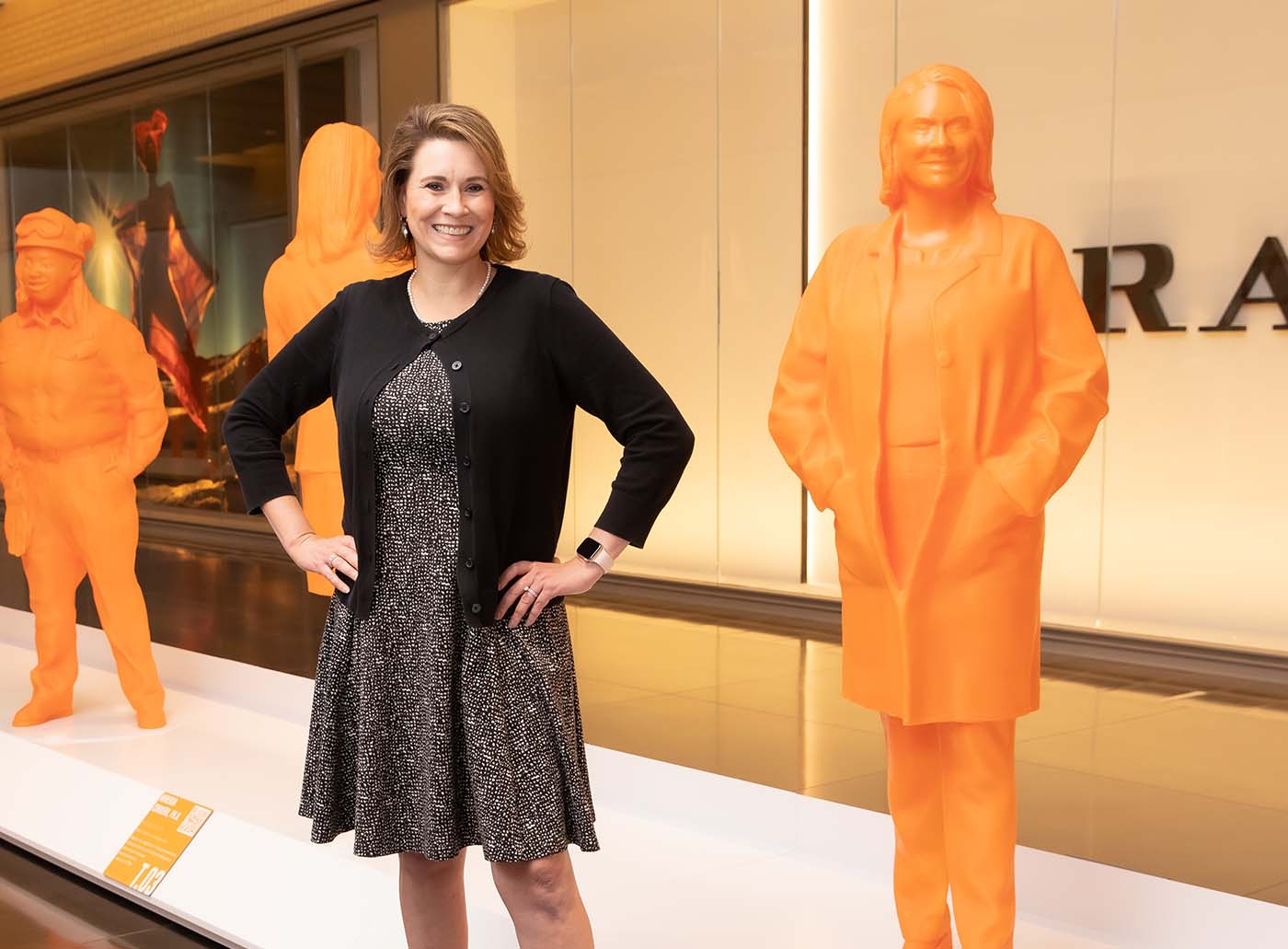 Woman in black jacket and spotted dress standing next to statue of herself
