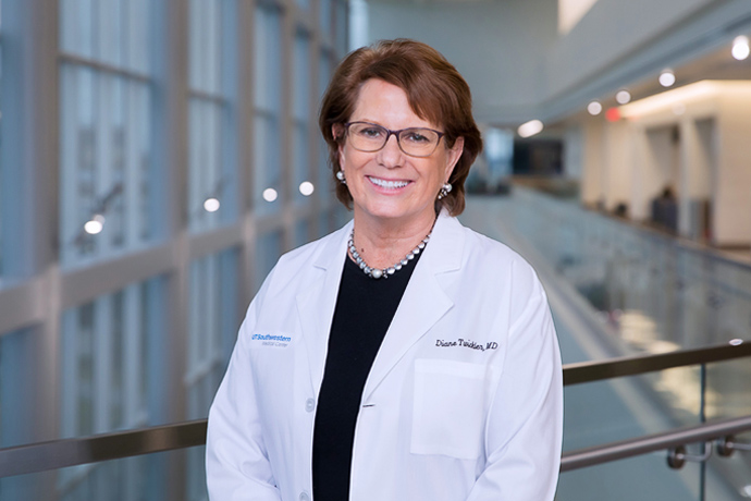 Woman with lab coat, brown hair, standing in front of windows