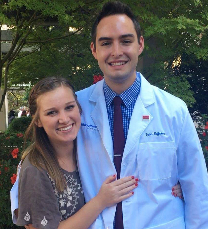 Man in white lab coat with woman in grey shirt, both smiling