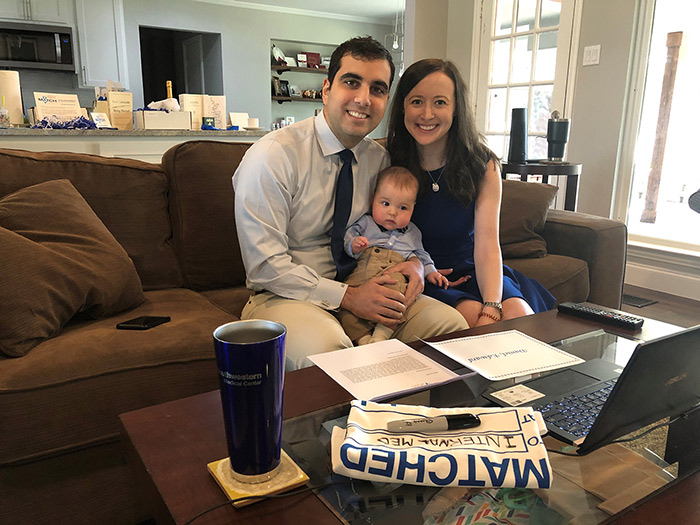 Two people smiling and holding a baby while sitting on a couch