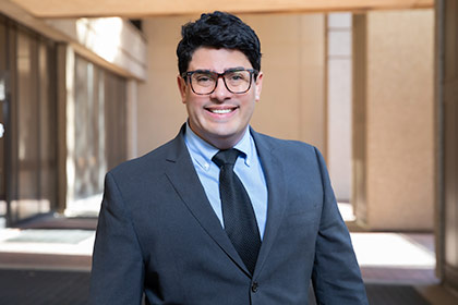 Man in grey suit, navy tie, with galases and black hair