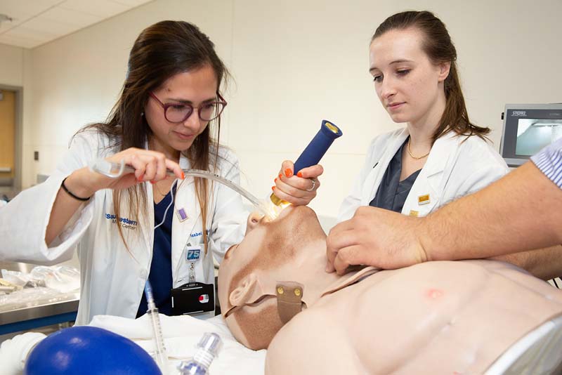 Woman in lab coat holding light and pushing tube down dummy's throat