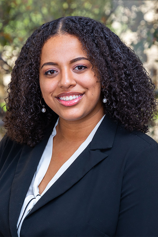 woman with short dark spiral curls wearing blue blazer over light blue shirt