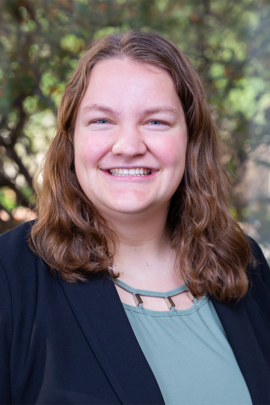 Woman with short dark hair, wearing navy suit jacket and blue top