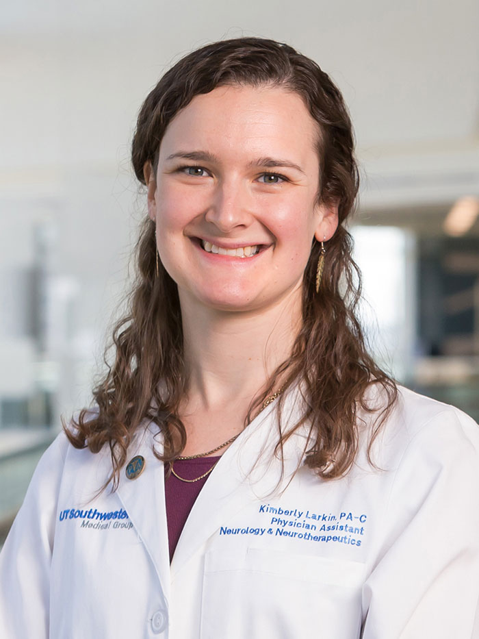 Woman with shoulder length reddish brown hair wearing burgundy shirt beneath white lab coat