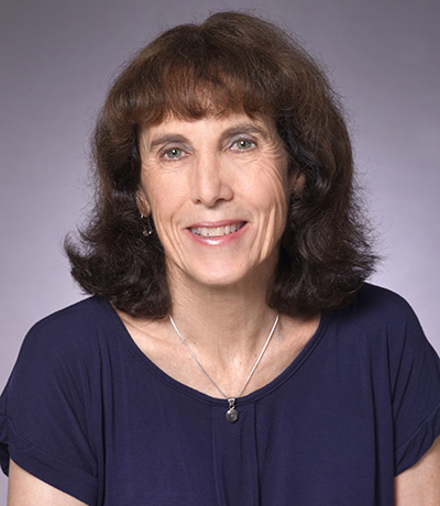 Woman with dark brown hair, wearing blue sweater and necklace