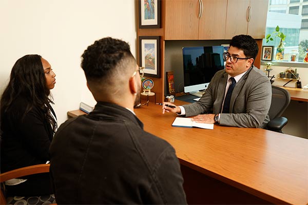 man sits at desk across from students 