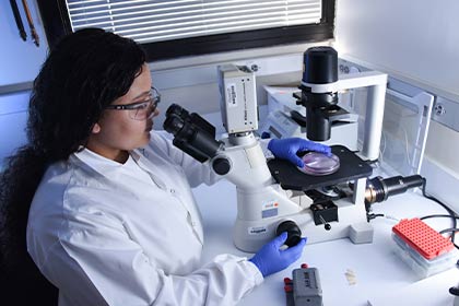 woman in lab coat sitting at desk with microscope