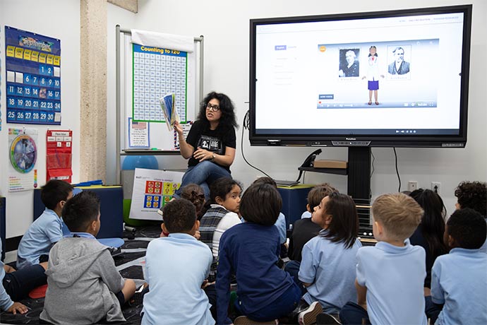 children seated on floor in front of teacher 