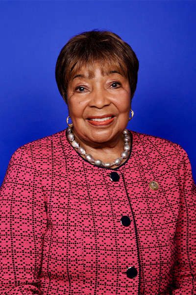 woman with short cropped hair wearing pink and black suit against blue background