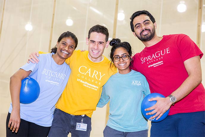 four students wearing different color t-shirts hold blue balls