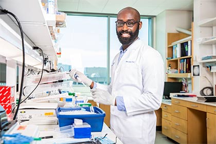 Man with dark beard and glasses wearing lab coat working in a lab