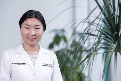 Dark-haired woman in lab coat standing next to indoor plant