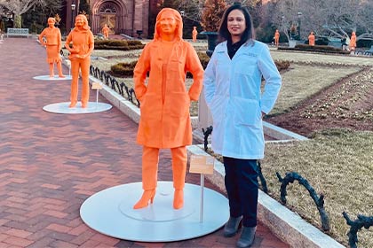 Woman in lab coat standing next to orange 3D print statue that looks like her in the courtyard of Pegasus Park