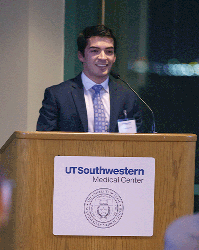 dark haired man speaks at podium to audience