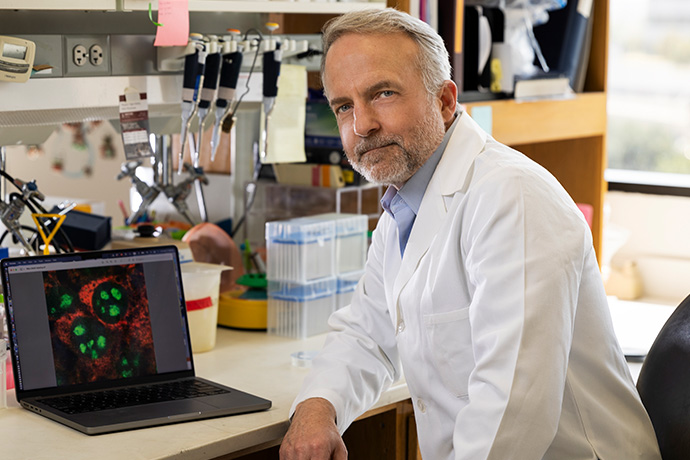 Dr. Buszczak, with gray hair and beard wearing a lab coat, in a lab.